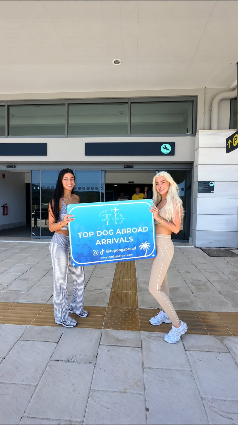 Two Top Dog Abroad arrivals holding a Top Dog Abroad Arrivals sign outside the airport on arrival day