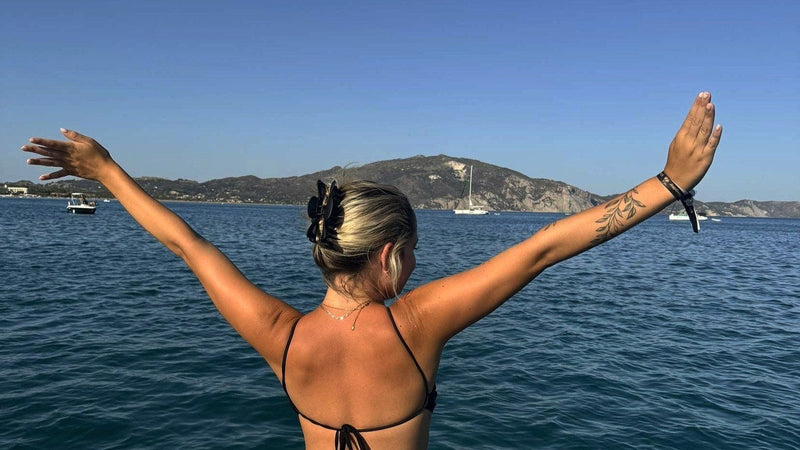 Caoimhe with her arms raised on the front of a boat, looking out across the sea off Zante